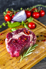 Raw marbled beef meet steak rib eye. Beef steak on the wooden plate with the rosemary and tomatoes