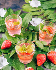 Homemade Strawberry liqueur on a metal table. Alcoholic fruit cocktail shots in a glasses. Green leafs