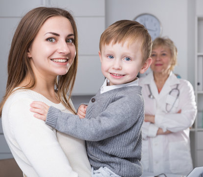 Smiling female is standing satisfied with her toddler after visiting clinic