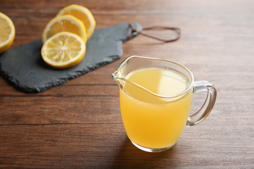 Glass jug with fresh lemon juice on wooden table