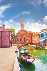 Fototapeta na wymiar Street with colored houses on the island of Burano and with a canal in the middle, near Venice, Italy. Parrocchia San Martino Vescovo