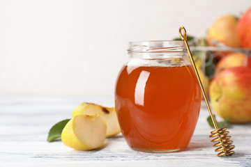 Jar of honey, apples and dipper on wooden table