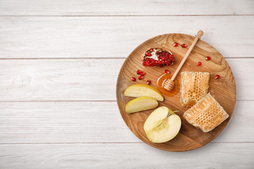 Flat lay composition with honey, dipper, sliced apples and pomegranate on wooden background. Rosh...