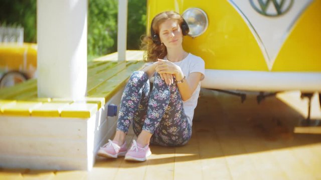 young woman outdoors by yellow vagon car listening music in headphones using smartphone - relaxing, enjoying, concept of technology and travel