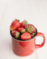 Bowl of strawberry on a wooden table. Fresh sweet berries in a red cup.