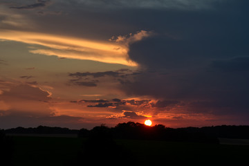 coucher de soleil sur la campagne avec les arbres en silhouette sur l'horizon. Le soleil rouge est sur l'horizon.