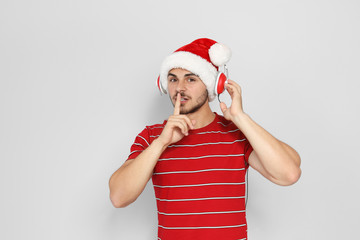 Young man in Santa hat listening to Christmas music on color background