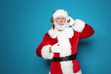 Fototapeta na wymiar Santa Claus listening to Christmas music on color background