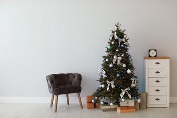 Stylish living room interior with decorated Christmas tree and comfortable armchair
