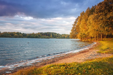 Autumn landscape of lake and colorful trees on shore in the evening. Yellow and red leaves on tree...