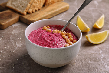Bowl with fresh beet hummus, slices of bread and lemon on table
