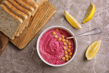 Flat lay composition with bowl of fresh beet hummus, slices of bread and lemon on gray background