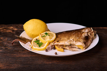 Appetizing baked fish, covered with juicy lemons, garlic and salt on side, above view