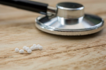 Stethoskop mit homöopathischen Kügelchen auf einem Holztisch