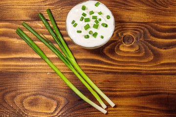 Sour cream and green onion on wooden table. Top view