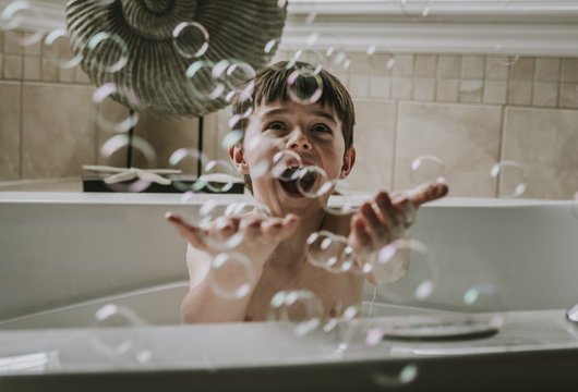Happy boy playing with bubbles while taking bath in bathtub