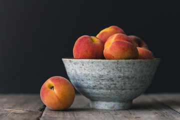 Close up of peaches in bowl on wooden table against black background