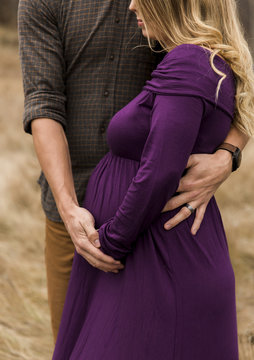 Midsection of husband embracing pregnant wife while standing outdoors