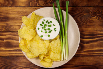Crispy potato chips with green onion and sour cream on wooden table. Top view