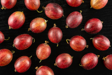 Lot of whole fresh red gooseberry hinnomaki variety flatlay on black wood