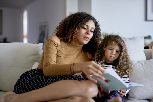 Mother reading picture book for daughter while sitting on sofa at home