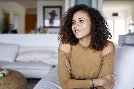 Happy Woman With Arms Crossed Looking Away While Sitting On Sofa At Home