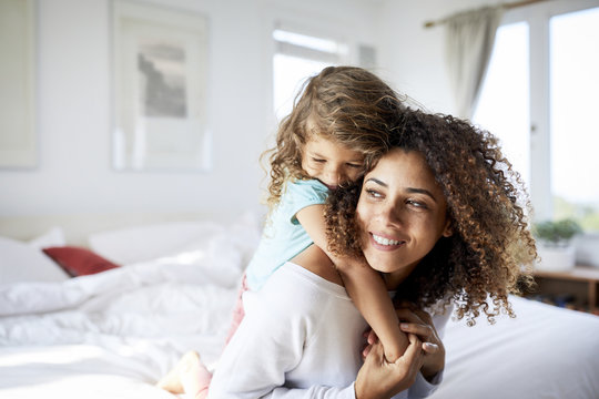 Happy daughter embracing mother sitting on bed at home