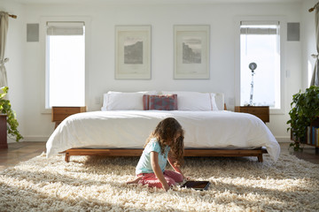 Side view of girl using tablet computer while sitting on rug in bedroom