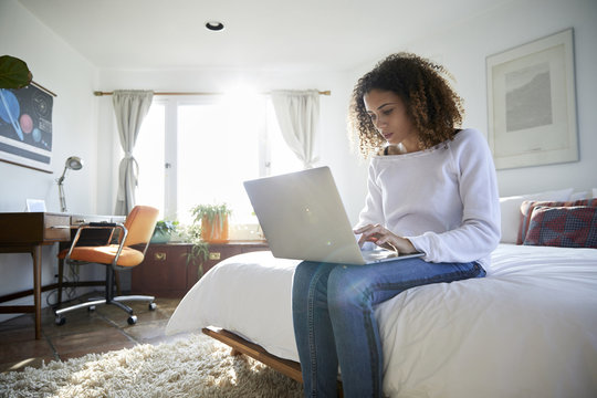 Low Angle View Of Woman Using Laptop Computer While Sitting On Bed At Home