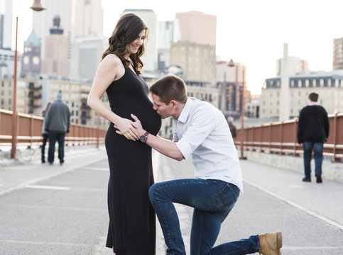 Husband kissing pregnant wife's stomach while standing on city street