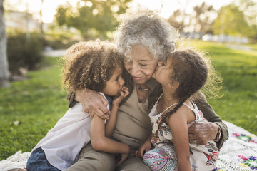 Grandchildren with grandmother on picnic blanket at park