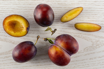 Group of three whole one half two slices of fresh violet-blue plum vibrant moyer variety flatlay on grey wood