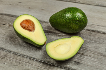 Avocado cut in half with whole green pear in background on rustic wood desk.