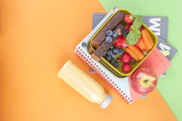 School lunch in a box and juice with fruit on a green background and a book. Free space for text. Copy space.