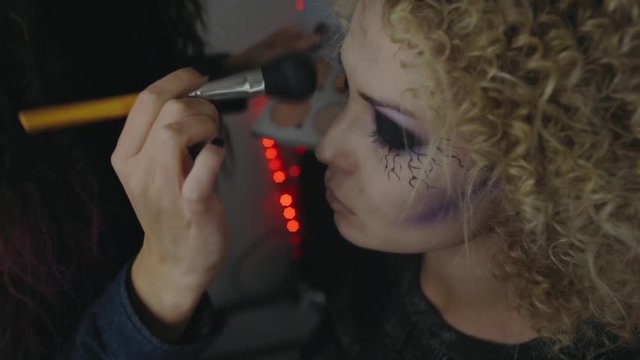 Halloween party, make-up artist draws a terrible makeup on the face of a brunette woman for a Halloween party