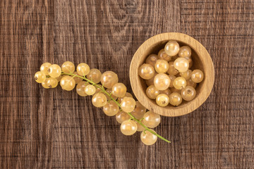 Fototapeta na wymiar Lot of whole fresh white currant berry blanka variety in a wooden bowl one strig flatlay on brown wood