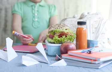 School lunch in a box and juice with fruit on a green background and books in the hands of a girl. Toast and juice in a bottle. Free space for text. Copy space.