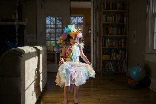 Full length of girl wearing colorful unicorn costume standing on hardwood floor at home