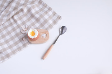 Served table for breakfast boild egg in wooden egg cup with salt spoon and checkered napkin White background Top view Minimalism Copy space