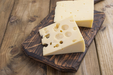 Dutch cheese with holes on a wooden old board. Vintage photo. Dairy. Free space for text. Copy space.