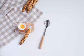 Served breakfast boiled egg in wooden egg cup with breadsticks salt spoon and checkered napkin White background Top view Minimalism Copy space