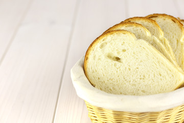 White sliced bread in a basket on the white wooden table.