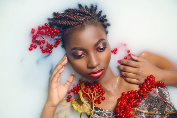 Glamorous African woman with bright make-up in milk with red berries top view close-up. The