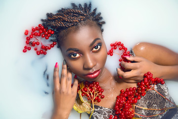 Glamorous African woman with bright make-up in milk with red berries top view close-up. The