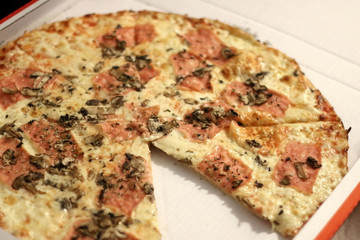 Ham, cheese and mushroom pizza in a box. One piece is cut out. Selective focus. 
