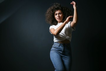 curly sexy beautiful woman is dancing and posing on a dark background. a brunette in fashionable...