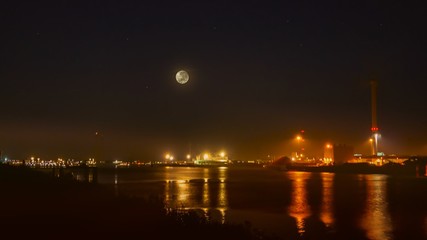 Fototapeta premium View of cargo port at night . View of the loading in the sea port . Cargo area on night time with reflections on water . eclipse of the moon 