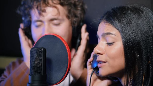 Two young singers performing their song in record studio. Professional musician duet recording new album CD. Beautiful couple working together. 4k