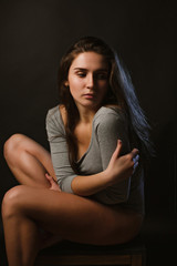 Tired sad brunette model sitting on a chair in the dark room