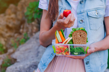Close up of young woman eating plum from lunch box filled with sandwich, fruits and vegetables